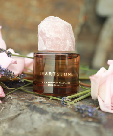 Tracy Anderson Fragrance's HeartStone Eau de Parfum resting on a rock surrounded by pink roses.