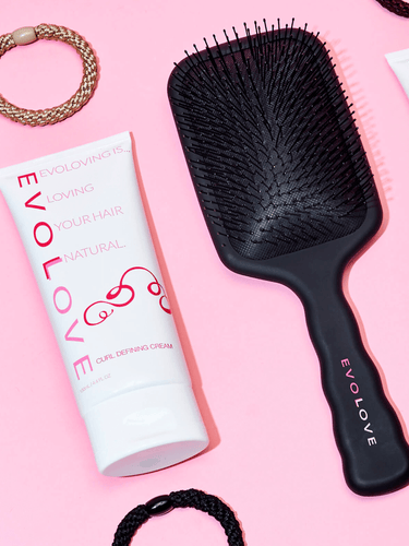 Curl defining cream and hair brush with hair ties lying next to each other.