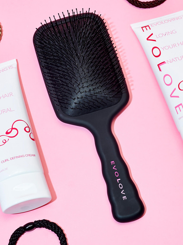 Curl defining cream and hair brush with hair ties lying next to each other.