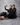 Famous twin influencers, Brittany and Briana Murillo, sitting down together in matching black outfits while holding their expensive-smelling celebrity perfume.